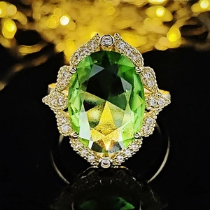 Elegant gold ring with oval green zircon and white crystal halo on black background