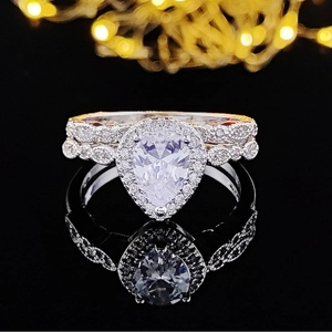 Primer plano de un conjunto de anillos con diamante de pera y halo sobre espejo negro