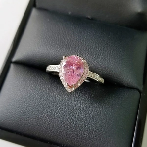 Macro di un anello con gemma rosa a forma di pera e diamanti incastonati su scatola nera