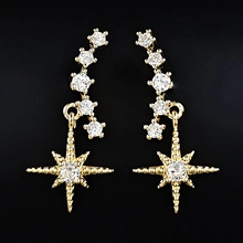 Detailed close-up of golden star-shaped earrings with white zircon on a black background