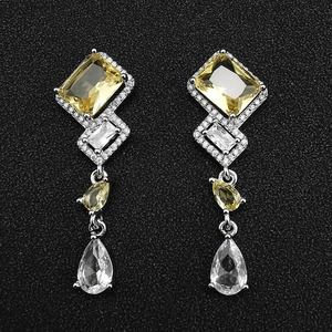 Geometric silver drop earrings with yellow and clear zircon stones on black background