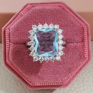Eleganter Ring mit hellblauem Saphir im Rechteckschliff und Diamantumrandung in Rosa Box