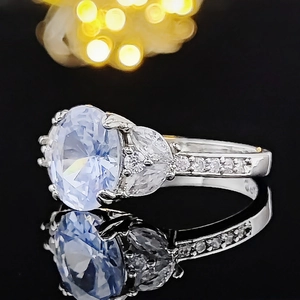 Anello d'argento elegante con grande pietra blu ovale e diamanti su superficie nera lucida