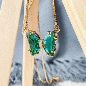 Detailed close-up of emerald green crystal butterfly pendant with gold box chain