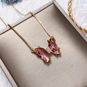Macro view of crystal butterfly pendant with pink gradient glass and gold chain detail