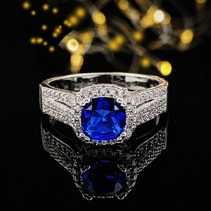 Anello di lusso con zaffiro taglio cushion e pavé di diamanti su sfondo nero lucido