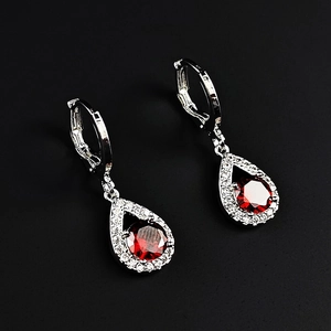 Détail de boucles d'oreilles en argent avec pendentif goutte, pierre rouge et halo de zircons
