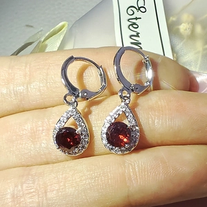 Gros plan sur des boucles d'oreilles argentées avec pierres rouges et halo de zircons