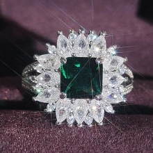 Macro shot of large emerald-cut green gemstone ring with radiant diamond halo detail
