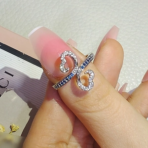 Macro shot of silver ring with zircon hollow heart design and blue gemstone on finger