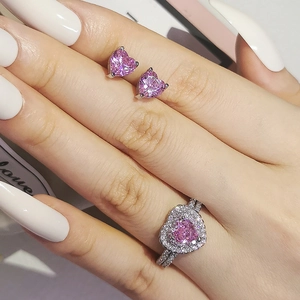 Parure bijoux avec bague et boucles d'oreilles cœur rose sur la main du modèle