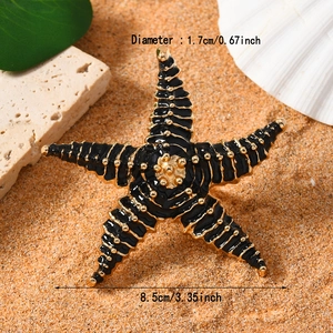 Dettaglio macro di un accessorio a stella marina dorata con smalto nero e misure di 8,5 cm