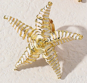 Macro di gioiello a forma di stella marina in smalto bianco con eleganti dettagli oro