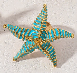 Dettaglio dell'anello a forma di stella marina con smalto blu e finiture dorate su pietra