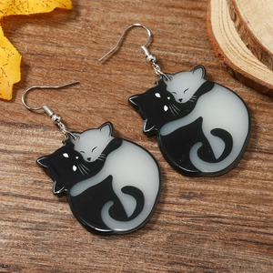 Macro detail of cute black and white hugging cat earrings on a natural wood background