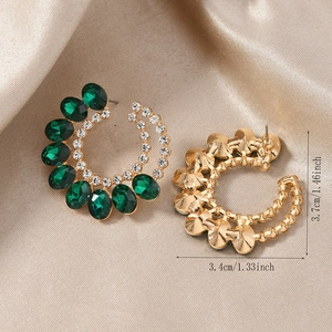 Détail de boucles d'oreilles dorées en C avec cristaux vert émeraude et strass blancs