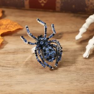 Dettaglio anello a ragno con strass blu su sfondo di legno e teschio decorativo