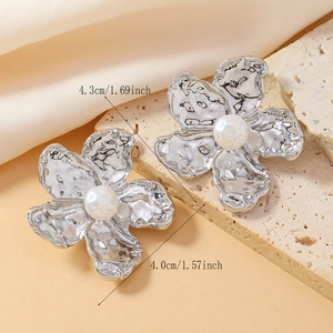 Détail de boucles d'oreilles fleurs argentées avec perle centrale et texture martelée