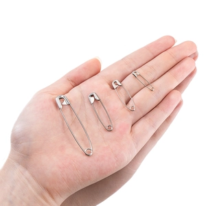 Polished stainless steel safety pins in four sizes displayed on a palm for scale