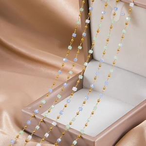 Detail of DIY stainless steel gold chain with pastel macaron beads on silk background