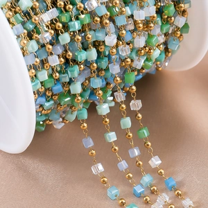 Macro shot of colorful crystal beads and gold metal chain on a white plastic spool