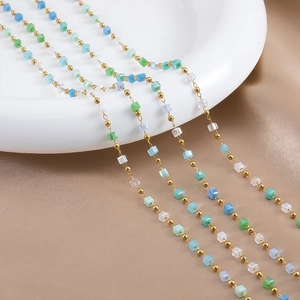 Close-up of golden stainless steel DIY chain with colorful square beads on white ceramic