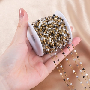 Macro detail of DIY gold chain with black, white and grey square beads on spool