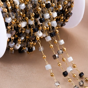 Close-up of gold beaded chain with black and white square beads on a white spool