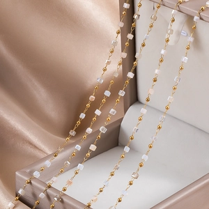 Detail of delicate gold ball chain with translucent white square beads on silk