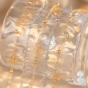Golden and silver butterfly link bracelets with beads draped on a wavy glass cup