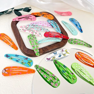 Assorted colorful teardrop snap hair clips with floral and animal prints on wood tray