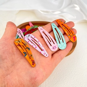 Close-up of colorful metal snap hair clips with cartoon prints held by hand