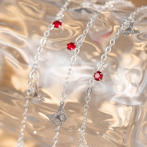 Silver chain necklace featuring butterfly charms and red crystal accents in a macro view