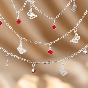 Detailed view of silver butterfly charms and red crystal drops on a layered chain