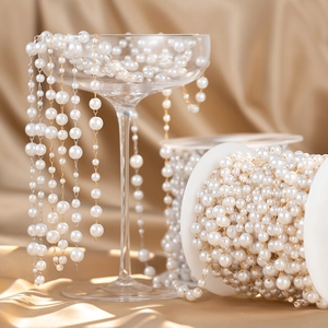 Detailed view of white pearl chain on champagne satin with elegant glassware presentation