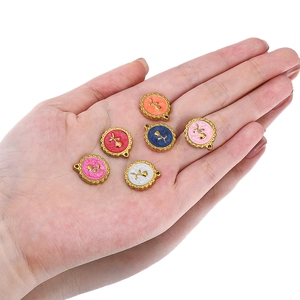 Set of 6 colorful enamel rose pendants with wavy gold edges shown on a palm for scale