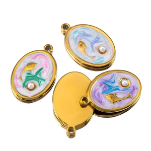 Macro view of oval gold charm with colorful enamel, swirling texture and white pearl inlay