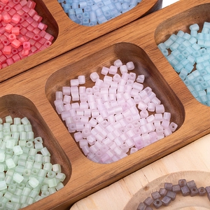 Macro detail of 4mm matte square glass seed beads organized in a wooden sorting tray