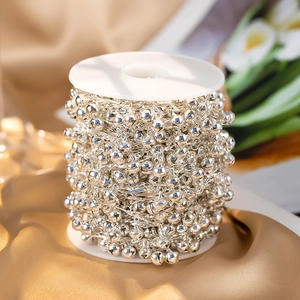 Makroaufnahme einer silbernen Glockenperlenkette auf Gold-Satin für DIY-Schmuck