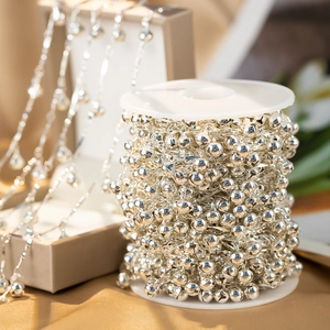 Makroaufnahme einer Rolle silberner Glockenketten auf goldenem Satin für DIY-Schmuck
