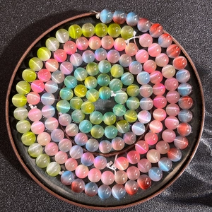 Makro-Detail von 8mm Regenbogen-Katzenaugenperlen spiralförmig auf einem Holztablett