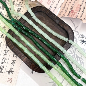 Bamboo shaped green glass beads displayed on a dark wooden tray with calligraphy