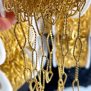 Macro detail of golden textured diamond-cut chain links on a white plastic spool