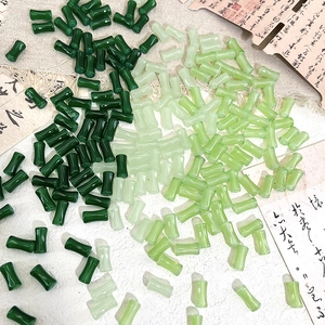 Bamboo shaped green glass beads for DIY jewelry making displayed on calligraphy paper