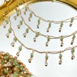 Detailansicht der goldenen Kette mit grünen Perlen und funkelnden Diamantanhängern auf Spiegel