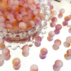 Macro shot of 8mm frosted Czech glass beads with orange-pink to purple gradient in glass bowl