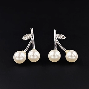 Gros plan sur des boucles d'oreilles cerise rétro avec feuilles argentées et perles
