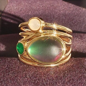 Macro shot of oval opal stone and green gemstones on layered gold rings in a velvet box