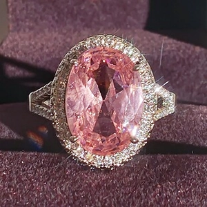 Close-up of luxury oval pink gemstone ring with halo diamonds on a purple background
