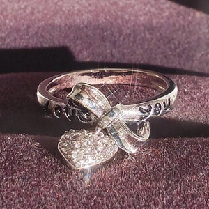 Macro shot of silver bow ring with heart pendant and LOVE YOU engraved on band